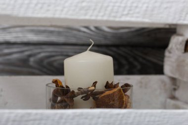 Cam şamdanda bir mum. Şamdan kurutulmuş koniler, baharatlar ve kurutulmuş meyvelerle dolu. Tahta bir kutunun içinde duruyor..