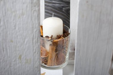 Cam şamdanda bir mum. Şamdan kurutulmuş koniler, baharatlar ve kurutulmuş meyvelerle dolu. Tahta bir kutunun içinde duruyor..