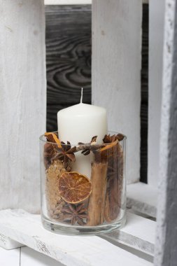 Cam şamdanda bir mum. Şamdan kurutulmuş koniler, baharatlar ve kurutulmuş meyvelerle dolu. Tahta bir kutunun içinde duruyor..