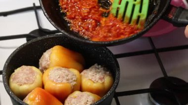 Bir adam dilimlenmiş et ve pirinçle doldurulmuş dolmalık dolma biber hazırlıyor. Sotelenmiş havuç ve ketçap ekliyor..