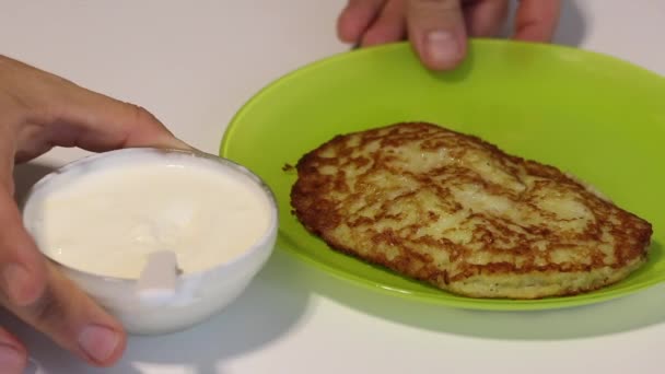 Připravená bramborová placka na talíři. Ten muž k tomu přidává kyselou smetanu.. — Stock video
