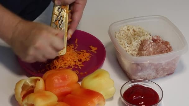 Seorang pria menyiapkan paprika diisi dengan daging cincang dan nasi. Memotong wortel di parutan — Stok Video