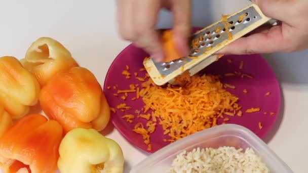 Um homem prepara pimentas recheadas com carne picada e arroz. Corta cenouras em um ralador. Imagem de close-up. — Vídeo de Stock