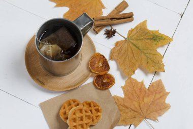 Bir fincan çay ve waffle. Masanın yanında kurumuş akçaağaç yaprakları, tarçın, anason ve kurutulmuş portakallar var. Sonbahar sakin bir hayat.