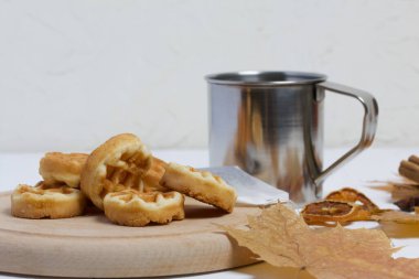 Bir fincan çay ve waffle. Masanın yanında kurumuş akçaağaç yaprakları, bir çay poşeti ve kurutulmuş portakallar var. Sonbahar sakin bir hayat.
