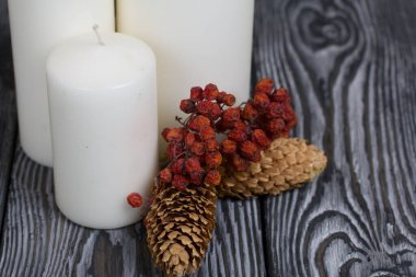 Boyalı çam ağaçlarının üzerinde üç beyaz mum duruyor. Spruce koniler ve kurutulmuş yaban mersinleri yakınlarda serilmiştir..