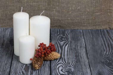 Boyalı çam ağaçlarının üzerinde üç beyaz mum duruyor. Spruce koniler ve kurutulmuş yaban mersinleri yakınlarda serilmiştir..