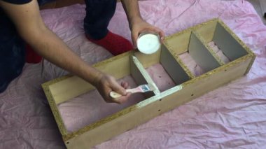 Bir adam ev yapımı bir raf boyuyor. Fırça ve beyaz boya. Genel plan.