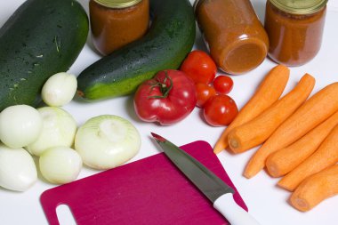 Kabak havyarı pişirmek için sebzeler. Kabak, havuç, soğan ve domatesler masanın yüzeyinde. Yakınlarda kabak havyarı kavanozları ve bıçaklı bir kesme tahtası var..
