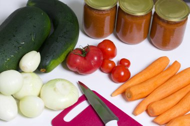 Kabak havyarı pişirmek için sebzeler. Kabak, havuç, soğan ve domatesler masanın yüzeyinde. Yakınlarda kabak havyarı kavanozları ve bıçaklı bir kesme tahtası var..