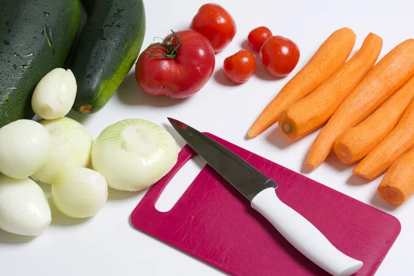 Vegetables for cooking squash caviar. Zucchini, carrots, onions and tomatoes on the table surface. Nearby is a cutting board with a knife.