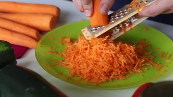 一个人把胡萝卜磨碎在磨子上.附近有蔬菜烹调南瓜鱼子酱.桌上有胡椒粉、胡萝卜、洋葱和西红柿.特写镜头 — 图库视频影像