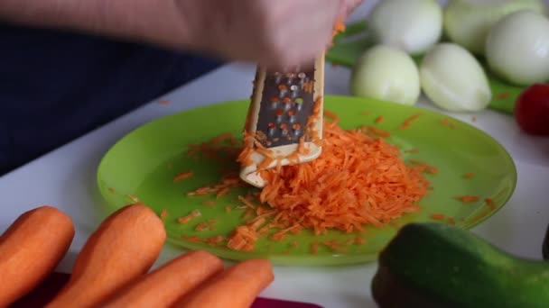 Мужчина шлифует морковь на терке. Ближайшие овощи для приготовления икры. Цуккини, морковь, лук и помидоры на поверхности стола. Крупный план. — стоковое видео