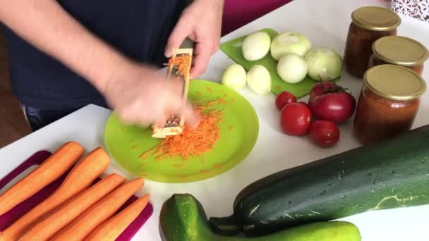 Człowiek mieli marchewkę na tarce. Pobliskie warzywa do gotowania kawioru squash. Cukinia, marchew, cebula i pomidory na powierzchni stołu. — Wideo stockowe