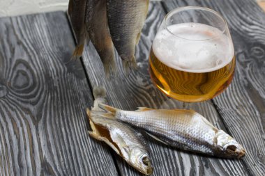 Kurutulmuş nehir balığı bir ipe tutunur. Yakınlarda bir bardak bira var..