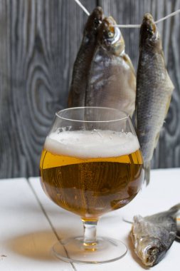 Kurutulmuş nehir balığı bir ipe tutunur. Yakınlarda bir bardak bira var..