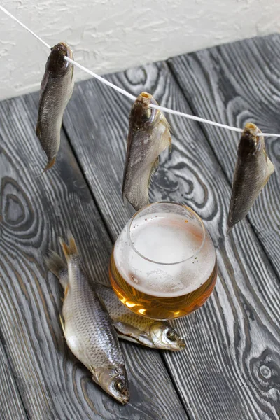 Dried river fish hangs on a rope. There is a glass of beer nearby.