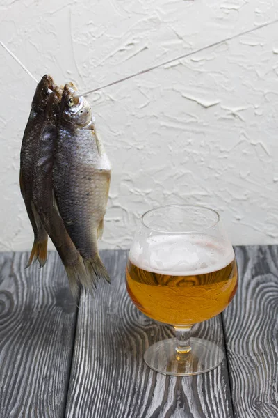 Dried river fish hangs on a rope. There is a glass of beer nearby.