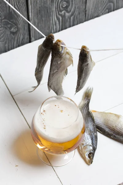 Dried river fish hangs on a rope. There is a glass of beer nearby.