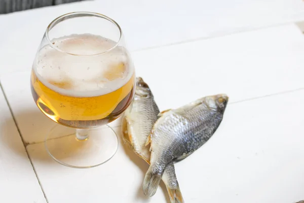 A glass of beer. Dried river fish lies nearby.