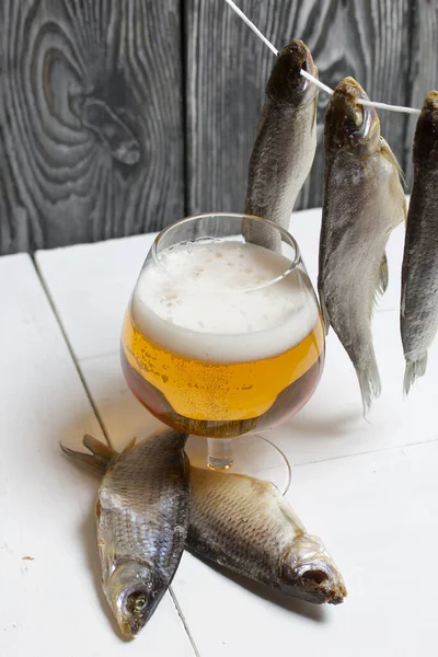 Dried river fish hangs on a rope. There is a glass of beer nearby.