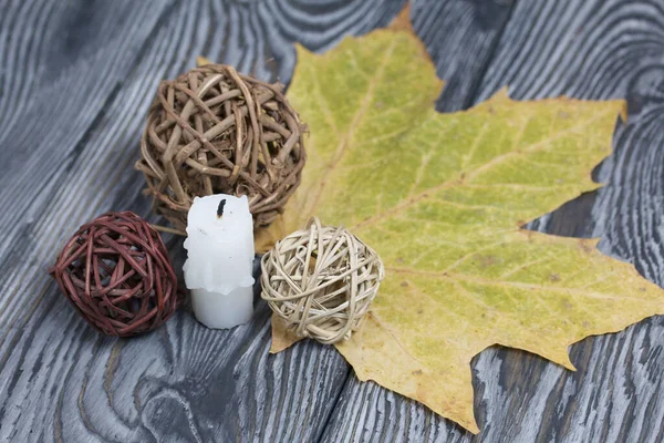 Candle stub on brushed pine boards. Nearby are dried maple leaves and rattan balls.