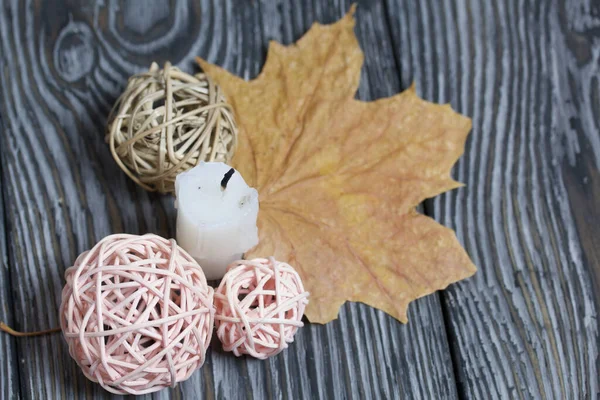 Candle stub on brushed pine boards. Nearby are dried maple leaves and rattan balls.