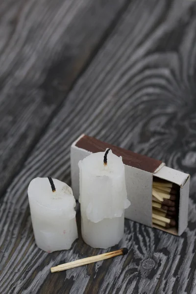 Two candlesticks on brushed pine boards. Beside a box of matches.