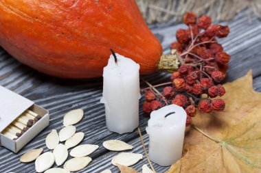 Portakal kabağı, tohumlar ve mum koçanları. Yakınlarda bir kutu kibrit, kurumuş akçaağaç yaprakları ve Rowan var. Çam ağacından yapılmış tahtalarda siyah beyaz boyanmış..