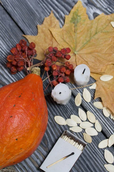 Portakal kabağı, tohumlar ve mum koçanları. Yakınlarda bir kutu kibrit, kurumuş akçaağaç yaprakları ve Rowan var. Çam ağacından yapılmış tahtalarda siyah beyaz boyanmış..