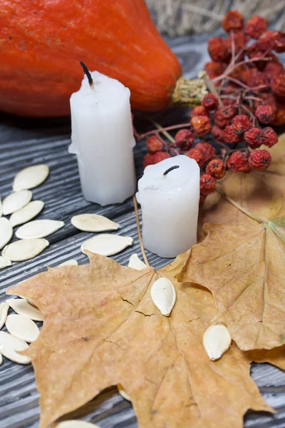 Portakal kabağı, tohumlar ve mum koçanları. Yakınlarda kurumuş akçaağaç ve Rowan yaprakları var. Çam ağacından yapılmış tahtalarda siyah beyaz boyanmış..