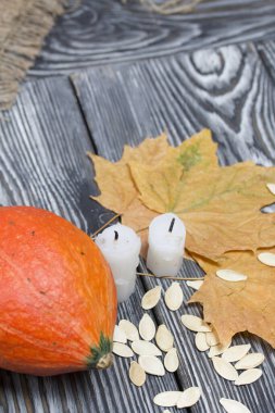 Portakal kabağı, tohumlar ve mum koçanları. Yakınlarda kurumuş akçaağaç yaprakları var. Çam ağacından yapılmış tahtalarda siyah beyaz boyanmış..