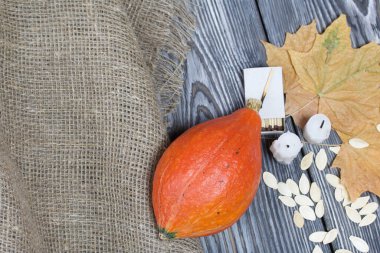 Portakal kabağı, tohumlar ve mum koçanları. Yakınlarda kibrit kutuları ve kurumuş akçaağaç yaprakları var. Çam ağacından yapılmış tahtalarda siyah beyaz boyanmış..