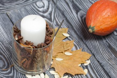 Portakal kabağı, tohumlar ve mum. Yakınlarda kurumuş akçaağaç yaprakları var. Çam ağacından yapılmış tahtalarda siyah beyaz boyanmış..