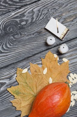 Portakal kabağı, tohumlar ve mum koçanları. Yakınlarda kibrit kutuları ve kurumuş akçaağaç yaprakları var. Çam ağacından yapılmış tahtalarda siyah beyaz boyanmış..