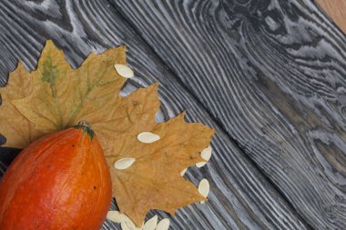 Portakal kabağı, tohumlar ve kurumuş akçaağaç yaprakları. Çam ağacından yapılmış tahtalarda siyah beyaz boyanmış..