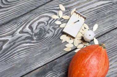 Portakal kabağı, tohumlar ve mum koçanı. Bir kutu kibritin yanında. Çam ağacından yapılmış tahtalarda siyah beyaz boyanmış..