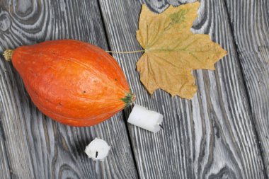 Turuncu balkabağı ve mum koçanları. Yakınlarda bir akçaağaç yaprağı var. Çam ağacından yapılmış tahtalarda siyah beyaz boyanmış..