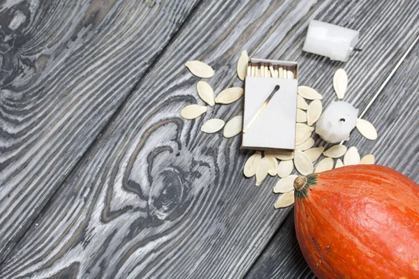 Portakal kabağı, tohumlar ve mum koçanı. Bir kutu kibritin yanında. Çam ağacından yapılmış tahtalarda siyah beyaz boyanmış..