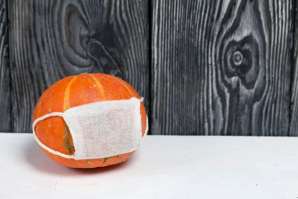 Orange pumpkin with a medical mask. Against the background of brushed pine boards, painted in black and white.