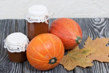 Kavanozda portakal kabağı ve balkabağı reçeli. Yakınlarda kurumuş akçaağaç yaprakları var. Çam ağacından yapılmış tahtalarda siyah beyaz boyanmış..