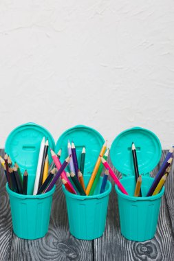 Kalem tutacaklarında renkli kalemler. Çöp tenekesi şeklinde bir kalem kutusu. Çam ağacından yapılmış tahtalarda siyah beyaz boyanmış..