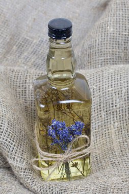 Bir şişe lavanta tentürü. Şişeye bir demet lavanta bağlanmış. Kaba ketenler üzerinde.