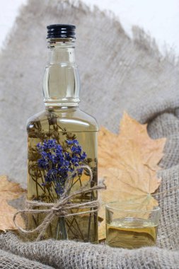 Bir şişe lavanta tentürü. Şişeye bir demet lavanta bağlanmış. Yakınlarda kurumuş akçaağaç yaprakları var. Kaba ketenler üzerinde. Yakın çekim..