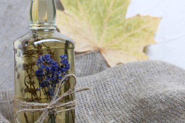 Bir şişe lavanta tentürü. Şişeye bir demet lavanta bağlanmış. Yakınlarda kurumuş akçaağaç yaprakları var. Kaba ketenler üzerinde. Yakın çekim..