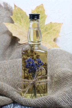 Bir şişe lavanta tentürü. Şişeye bir demet lavanta bağlanmış. Yakınlarda kurumuş akçaağaç yaprakları var. Kaba ketenler üzerinde. Yakın çekim..