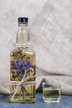 Bir şişe lavantalı votka. Şişeye bir demet lavanta bağlanmış. Yakınlarda bir bardak içki var. Alabildiğine yemyeşildirler..