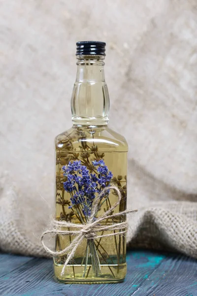 A bottle of lavender vodka. A bouquet of lavender is tied to the bottle. On black-green pine planks.