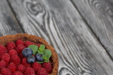 Krem peynirli fırınlanmamış çikolatalı kek. Ahududu, yaban mersini ve nane yapraklarıyla süslenmiş. Çam ağaçlarının yüzeyinde siyah beyaz boyanmış..