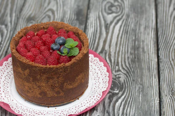 クリームチーズでチョコレートケーキを焼きません ラズベリー ブルーベリー ミントの葉で飾られています 黒と白で描かれた松の板の表面に — ストック写真